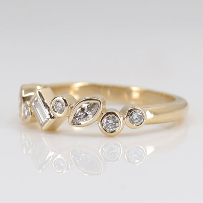 A stylish gold ring featuring assorted diamond shapes, including marquise, round emerald cut, set in a delicate bezel alternating design shown from the side.