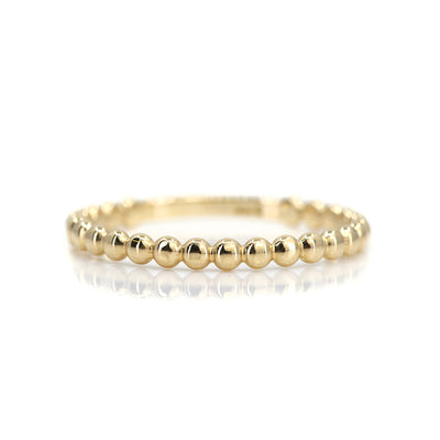 A simple gold beaded stacking ring resting on a white reflective surface. Perfect to stack everyday. 