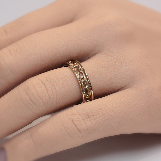 A decorative gold band ring featuring intricate cut-out designs and small spherical accents, reflecting light beautifully worn on a finger.