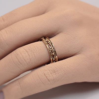 A decorative gold band ring featuring intricate cut-out designs and small spherical accents, reflecting light beautifully worn on a finger.