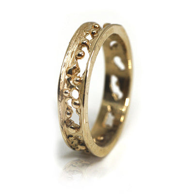 A decorative gold band ring featuring intricate cut-out designs and small spherical accents, reflecting light beautifully shown from the side.