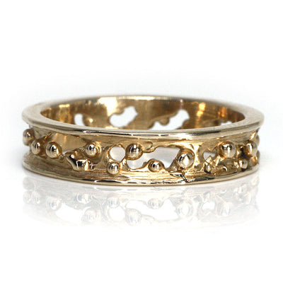 A decorative gold band ring featuring intricate cut-out designs and small spherical accents, reflecting light beautifully.
