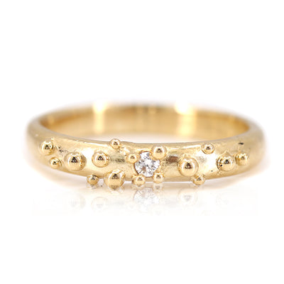 Gold ring with small bubble textures and a central diamond, reflecting a unique and contemporary design.