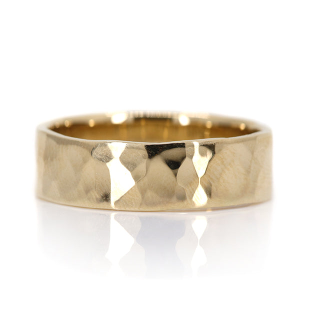 A polished gold ring with a hammered finish, showcasing a textured surface and a smooth interior, set against a white background.