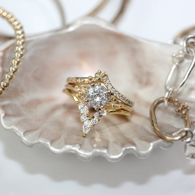 A stunning diamond engagement ring set in gold, embellished with smaller diamonds, resting on a delicate shell dish among other jewelry.