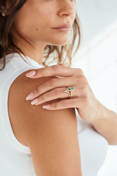 A green sapphire marquise engagement ring stacked with a diamond peaked wedding band worn by a model with short brown hair, posing elegantly.