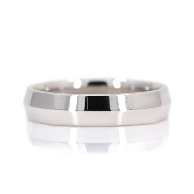 A polished, white gold knife edge wedding band with subtle shine, resting on a reflective surface.