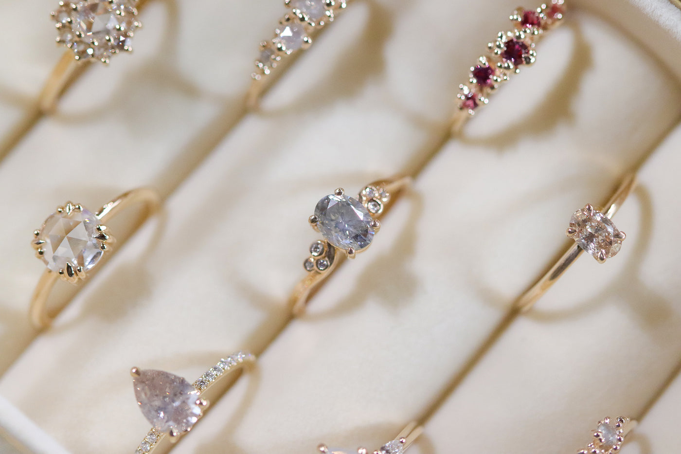 A collection of elegant gold rings with various gemstone settings displayed in a cream velvet box.