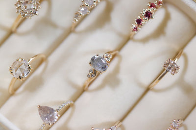 A collection of elegant gold rings with various gemstone settings displayed in a cream velvet box.