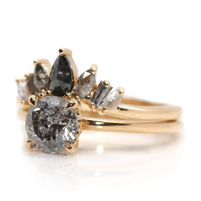 An elegant gold ring featuring a crown-like design with five diamonds in an ombre colour gradient, from black to salt & pepper to white diamonds stacked and shown from the side with a salt & pepper round diamond solitaire engagement ring.