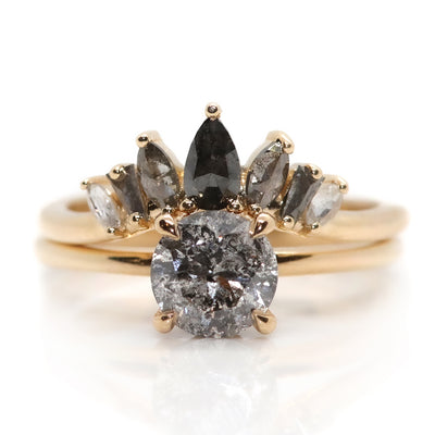 An elegant gold ring featuring a crown-like design with five diamonds in an ombre colour gradient, from black to salt & pepper to white diamonds stacked with a salt & pepper diamond round solitaire engagement ring. 