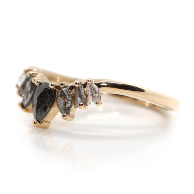 An elegant gold ring featuring a crown-like design with five diamonds in an ombre colour gradient, from black to salt & pepper to white diamonds. Shown resting upside down on a white surface.