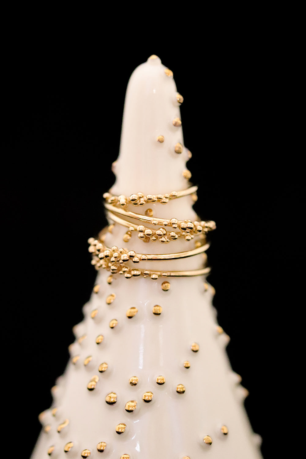 5 gold stacking rings are displayed on a smooth, white, cone shaped jewelry holder adorned with small golden beads.