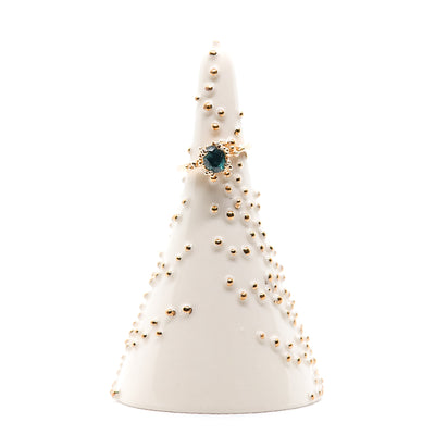 One blue sapphire ring is displayed on a smooth, white, cone shaped jewelry holder adorned with small golden beads.