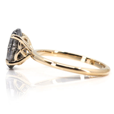 An elegant gold ring set with a large oval salt and pepper diamond. It features tiger-style prongs atop a decorative under basket, displayed on a white background. 