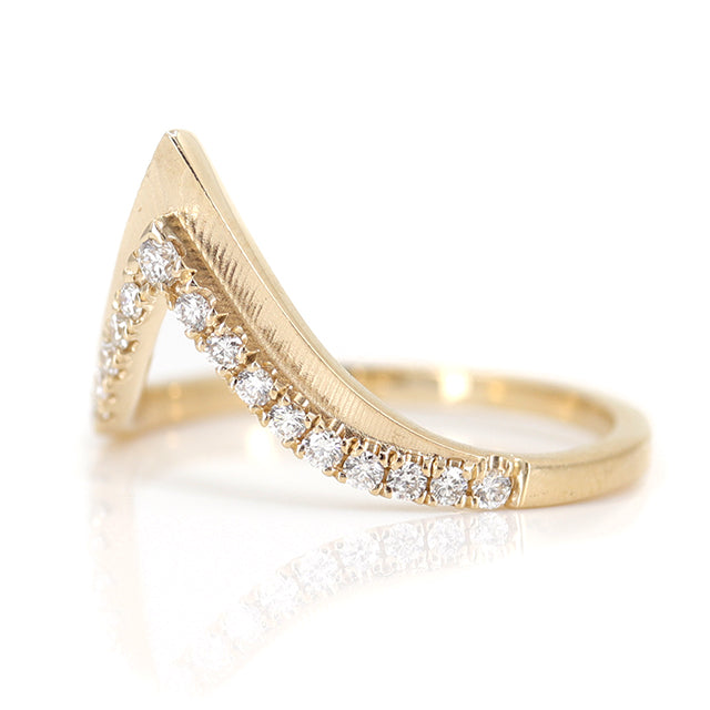 Elegant gold ring with a V-shaped design, encrusted with sparkling diamonds along the band on a white surface shown from the side.