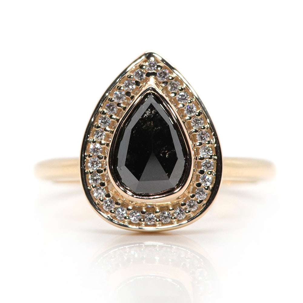 A pear-shaped black diamond ring is set in gold, surrounded by a halo of small, sparkling white diamonds. On a white background. 