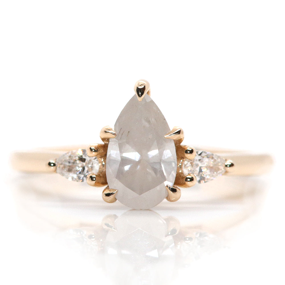 A three stone ring with a central fancy white pear-shaped diamond set in gold , flanked by two smaller pear diamonds, on a white background.