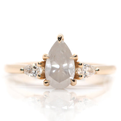 A three stone ring with a central fancy white pear-shaped diamond set in gold , flanked by two smaller pear diamonds, on a white background.