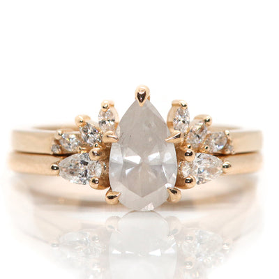 A three stone ring with a central fancy white pear-shaped diamond set in gold , flanked by two smaller pear diamonds, paired with an open diamond band, displayed on a white background.