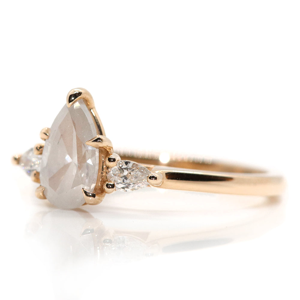 A three stone ring with a central fancy white pear-shaped diamond set in gold , flanked by two smaller pear diamonds, on a white background.