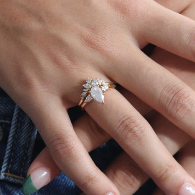 A three stone ring with a central fancy white pear-shaped diamond set in gold , flanked by two smaller pear diamonds, paired with a multi-shaped diamond band, worn together on a hand.