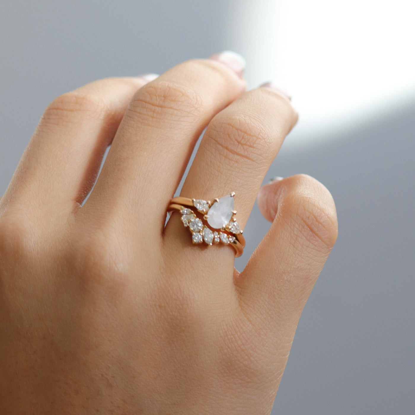 A three stone ring with a central fancy white pear-shaped diamond set in gold , flanked by two smaller pear diamonds, paired with a multi-shaped diamond band, worn together on a hand.