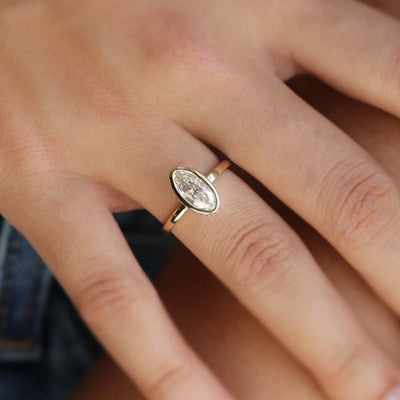 An elongated marquise-cut diamond ring bezel set with a polished gold band sits elegantly on a hand.