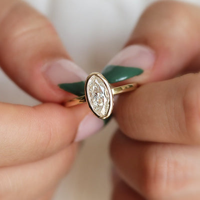 An elongated marquise-cut diamond ring bezel set with a polished gold band, shown held between two hands. 