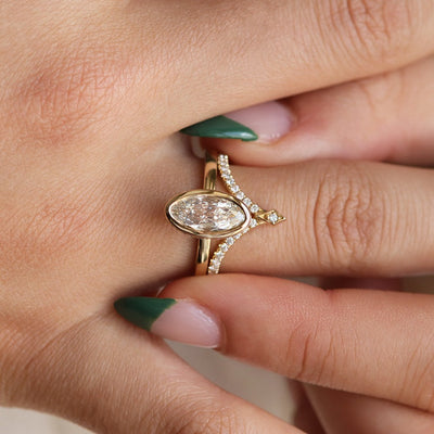 An elongated antique marquise-cut diamond ring bezel set with a polished gold band, paired with a 'V' pave diamond, sits elegantly on a hand.