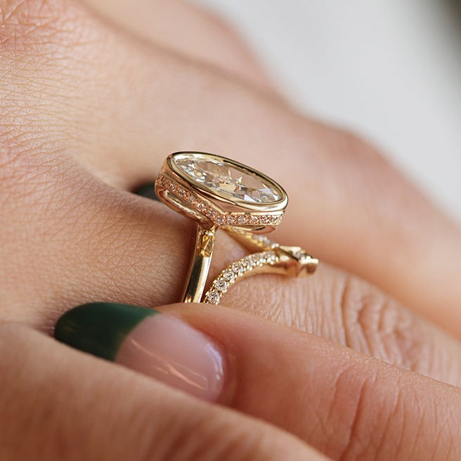 An elongated antique marquise-cut diamond ring bezel set with a polished gold band, paired with a 'V' pave diamond, sits elegantly on a hand.
