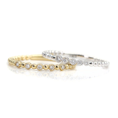 Two elegant white gold and yellow gold rings featuring alternating shiny beads and five sparkling diamonds, resting together set against a white background.