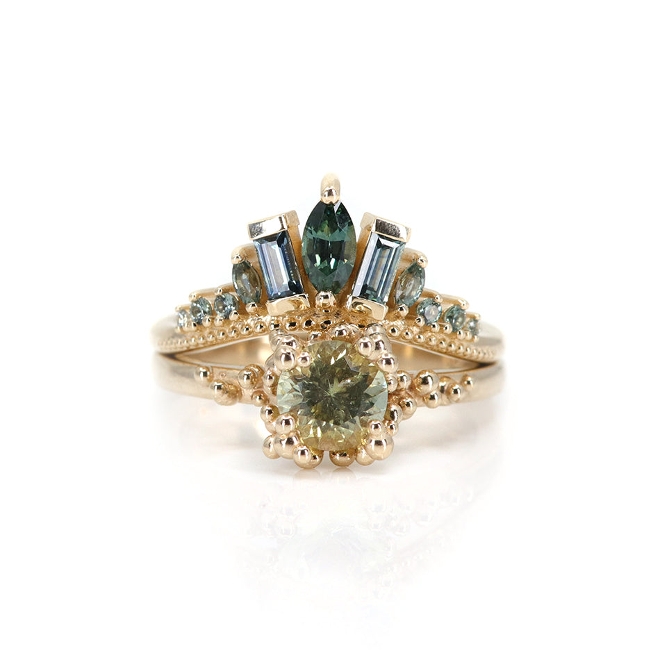 A delicate gold ring adorned with blue and teal sapphires, featuring a central marquise stone and two rectangular stones, stacked with a round solitaire baleal ring.