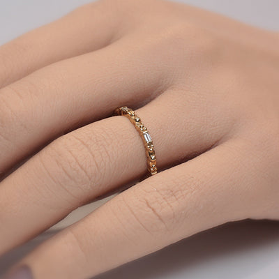 A delicate golden ring featuring alternating round and baguette-shaped stones, reflecting light with elegant simplicity worn on a finger.