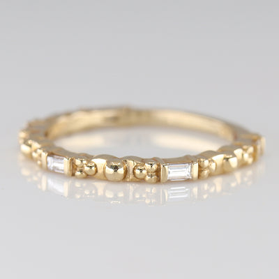 A delicate gold ring featuring alternating round and baguette-shaped stones, reflecting light with elegant simplicity.
