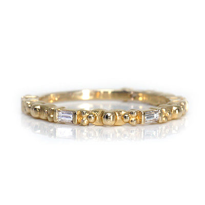A delicate gold ring featuring alternating round and baguette-shaped stones, reflecting light with elegant simplicity.