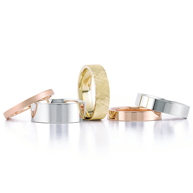 A collection of simple and elegant wedding bands in a variety of metals including yellow gold, rose gold and white gold. They vary in thickness and one has texture added to the band.
