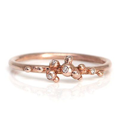 A delicate rose gold ring featuring a unique organic design with small bead-like accents and sparkling diamonds.
