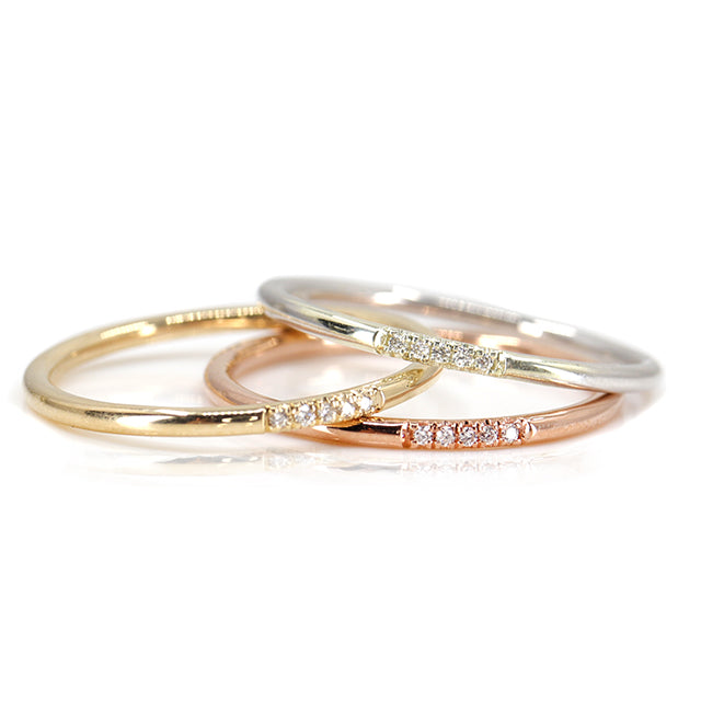 Simple and elegant stacking rings with rounded bands in different types of gold, all with 5 pave diamonds, sparkle on a white surface.