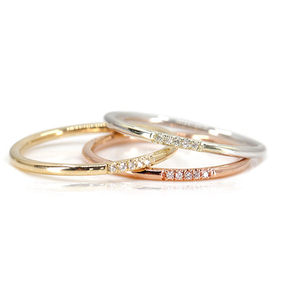 Simple and elegant stacking rings with rounded bands in different types of gold, all with 5 pave diamonds, sparkle on a white surface.
