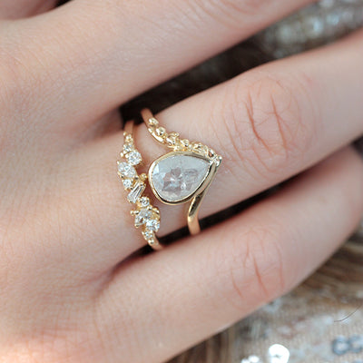 Yellow Gold ring with diamonds clustered across the band in various shapes like round, marquise and baguette on a finger stacked with a white diamond pear shaped unique engagement ring.