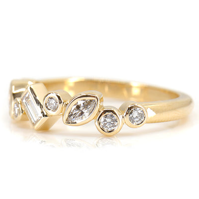 A stylish gold ring featuring assorted diamond shapes, including marquise, round emerald cut, set in a delicate bezel alternating design shown from the side.