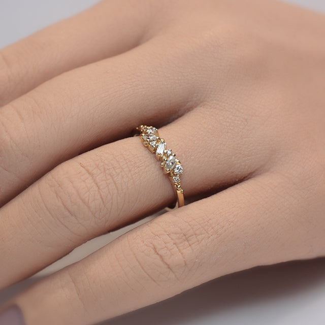 Yellow Gold ring with diamonds clustered across the band in various shapes like round, marquise and baguette worn on a finger.