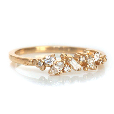 Yellow Gold ring with diamonds clustered across the band in various shapes like round, marquise and baguette on a white background.