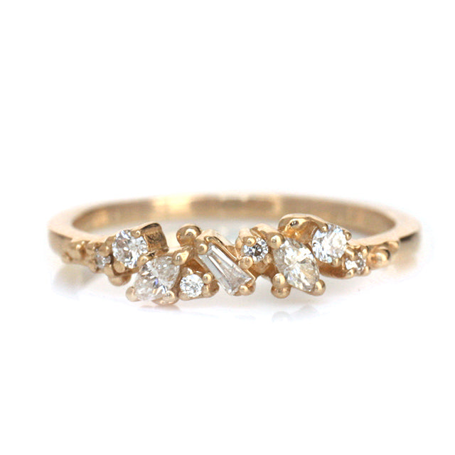 Yellow Gold ring with diamonds clustered across the band in various shapes like round, marquise and baguette on a white background.