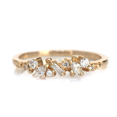 Yellow Gold ring with diamonds clustered across the band in various shapes like round, marquise and baguette on a white background.