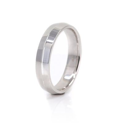 A polished, white gold knife edge wedding band with subtle shine, resting on a reflective surface.