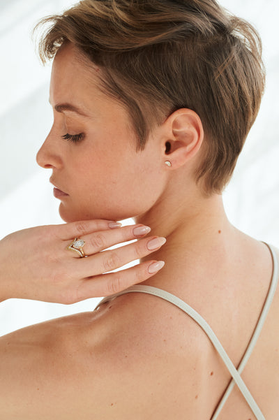 Elegant gold ring with a V-shaped design, encrusted with sparkling diamonds along the band, stacked with a marquise diamond engagement ring worn by a model elegantly turned away from the camera.