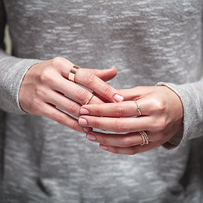 A woman holding her hands loosely together wearing various yellow and rose gold rings together, some plain bands and some with tiny gemstones.