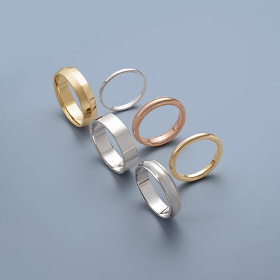 Six rings in various metals such as yellow gold, white gold and white gold. They rest on their side and vary in style from a curved band, flat edge or knife edge.